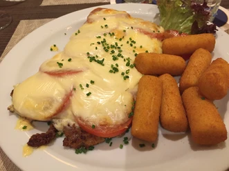 Een ovengebakken schnitzel met tomaten, gesmolten kaas en kroketten op een bord.