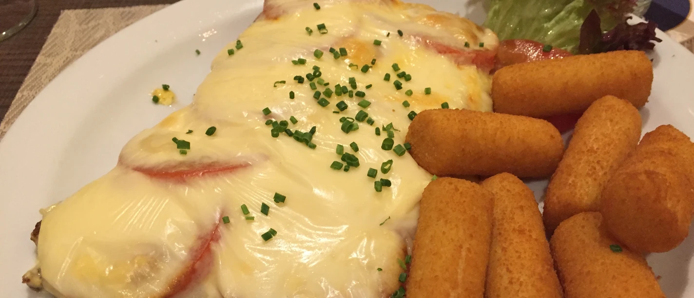 Schnitzelgericht Ein im Ofen gebackenes Schnitzel mit Tomaten, geschmolzenem Käse und Kroketten auf einem Teller.