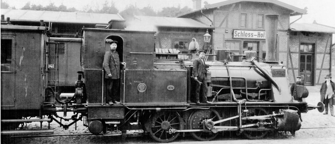 Bahnhof 1 1906-Lokomotive-im-1024x496.jpg Historische Dampflokomotive von 1906 mit Bahnpersonal am Bahnhof Schloß Holte.