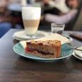 A slice of succulent cake lies on a plate next to a coffee drink in a café atmosphere.