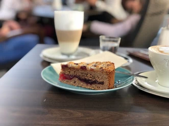 Kuchen Ein Stück saftiger Kuchen liegt auf einem Teller neben einem Kaffeegetränk in einem Café-Ambiente.