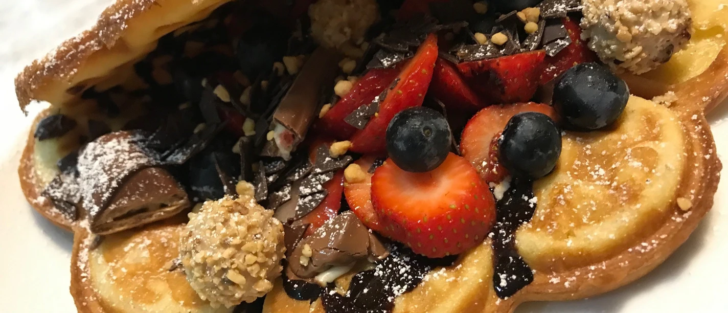 Waffel gefüllt Waffel mit Schokoladencreme, gefüllt mit frischen Erdbeeren, Blaubeeren und Pralinen, auf Teller.