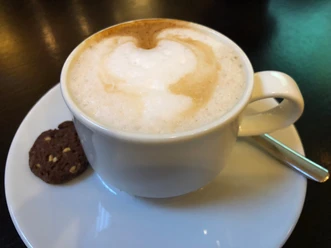 Cappuccino with rich milk foam and cookie on a white saucer, viewed slightly from above.