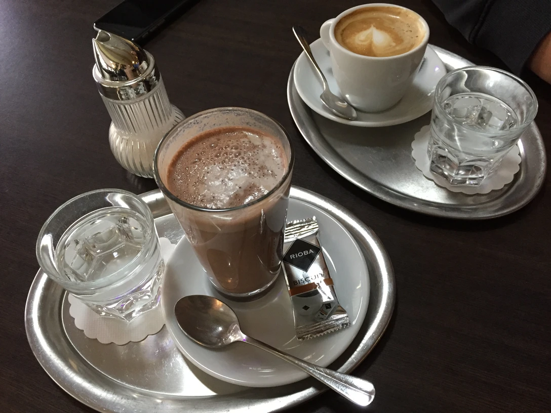 Kaffee Ein Tablett auf dunklem Tisch mit einem Cappuccino, einem Glas Wasser und einem Schokoladengetränk.