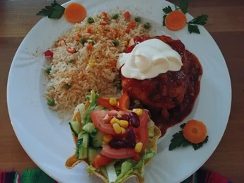 mexikanisches Essen Ein Teller mit mexikanischem Reis, überbackenem Hähnchen und frischem Salat, dekoriert mit Karottenscheiben.