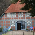 Fachwerkhaus aus rotem Backstein mit blauen Holzbalken und bunten Kunstwerken auf einer grünen Wiese.