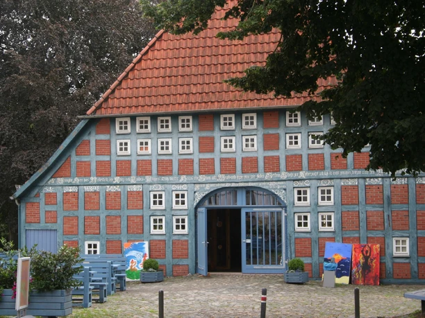 Clüverhaus Fachwerkhaus aus rotem Backstein mit blauen Holzbalken und bunten Kunstwerken auf einer grünen Wiese.