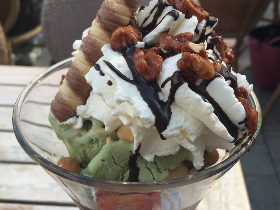 Ein köstlicher Eisbecher mit Sahne, Schokoladensoße, Nüssen und zwei knusprigen Schokoröllchen.