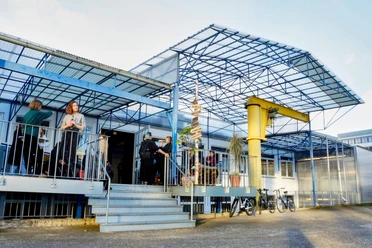 TanzFaktur - Außenansicht Außenbereich der TanzFaktur mit blauem Stahlgerüst, Treppe, Gästen und Fahrrädern