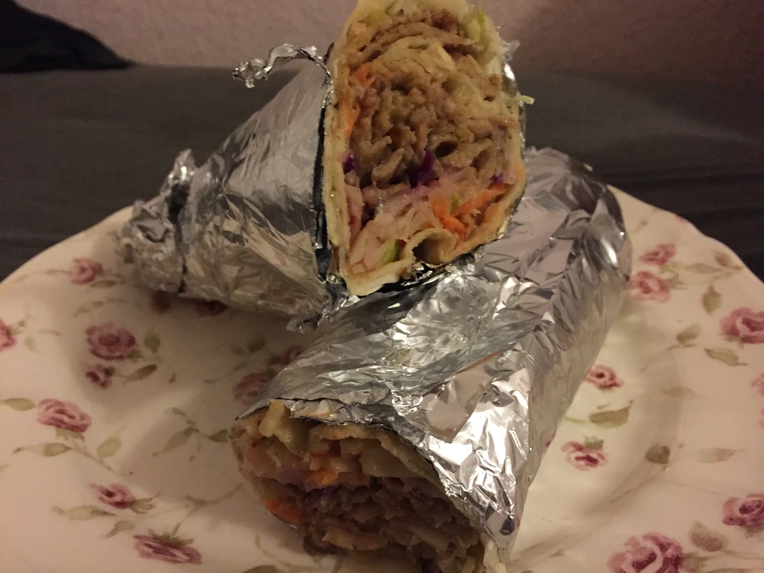 Döner Rollo Ein auf einem Teller platzierter Döner Rollo, gefüllt mit saftigem Fleisch und frischem Gemüse.