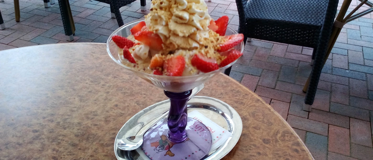 A strawberry sundae with cream and crunchy nut crumble is served on a terrace.