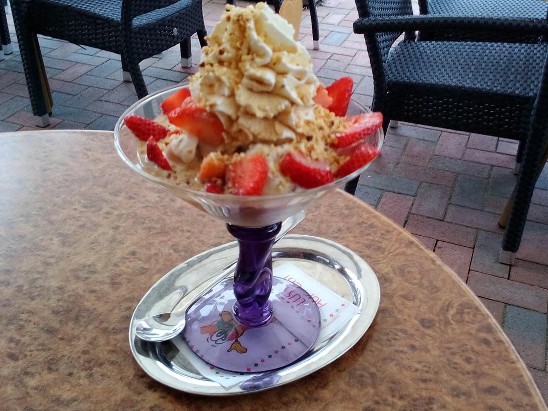 Erdbeer Eisbecher Ein Erdbeer-Eisbecher mit Sahne und knusprigen Nussstreuseln wird auf einer Terrasse serviert.A strawberry sundae with cream and crunchy nut crumble is served on a terrace.En jordbærsundae med fløde og knasende nøddecrumble serveres på en terrasse.Een aardbeienijsje met room en krokante notencrumble wordt geserveerd op een terras.