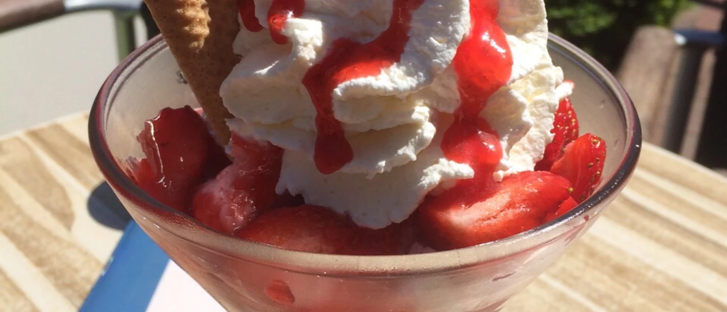 Eisbecher Erdbeer-Eisbecher mit Sahne, Erdbeeren, Waffeln und Soße in einem Café an einem sonnigen Tag.