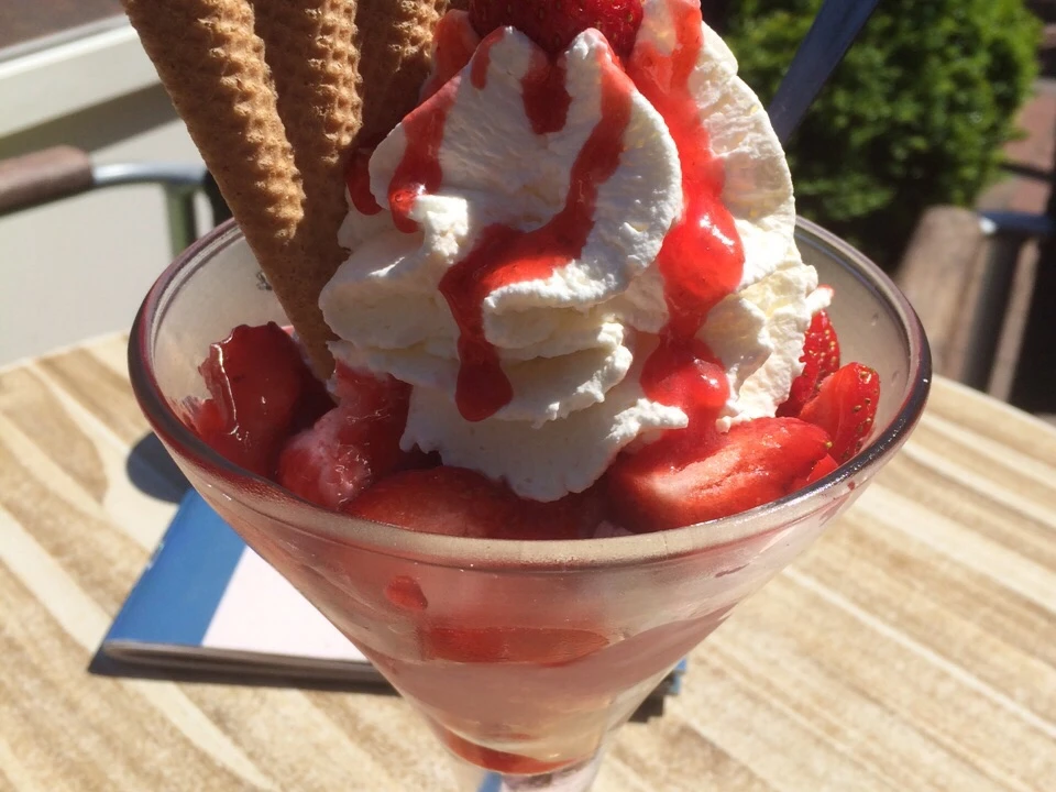 Eisbecher Erdbeer-Eisbecher mit Sahne, Erdbeeren, Waffeln und Soße in einem Café an einem sonnigen Tag.Strawberry sundae with cream, strawberries, waffles and sauce in a café on a sunny day.Jordbærsundae med fløde, jordbær, vafler og sauce på en café på en solrig dag.Aardbeienijs met slagroom, aardbeien, wafels en saus in een café op een zonnige dag.