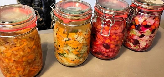 Vier Bügelgläser mit bunt fermentiertem Gemüse auf einer Arbeitsfläche