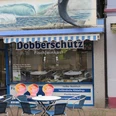 Dobberschütz Ein Fischgeschäft mit blauer Markise und einem großen Fisch an der Wand. Davor stehen Tische und Stühle.