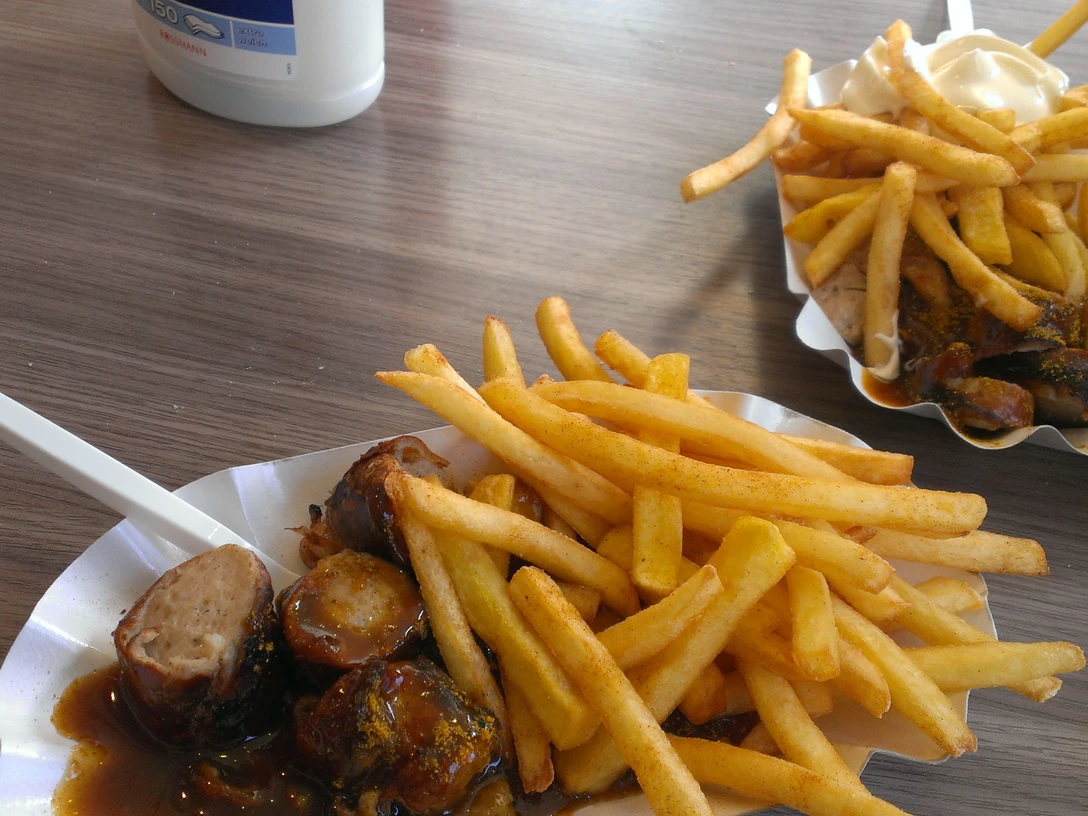 Leckere Currywurst mit knusprigen Pommes, serviert in einer Pappschale mit Plastikgabel.