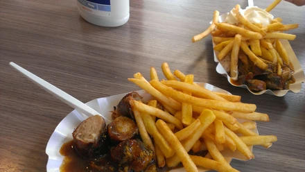 Currywurst Pommes Leckere Currywurst mit knusprigen Pommes, serviert in einer Pappschale mit Plastikgabel.