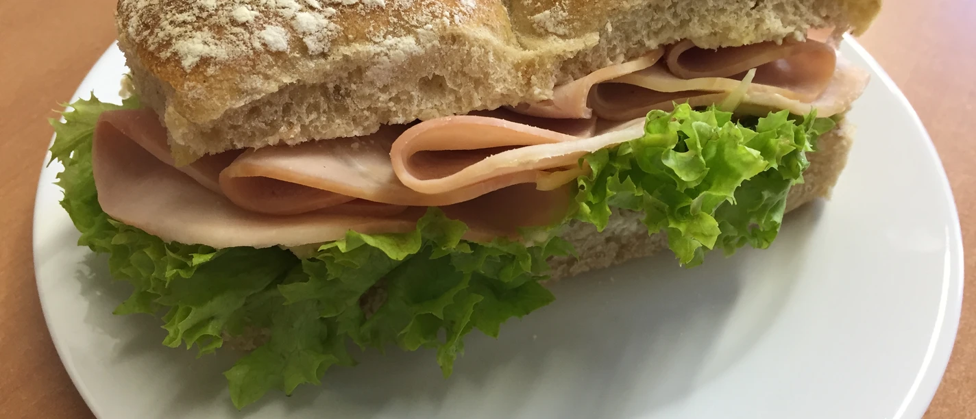 Belegtes Brötchen Ein belegtes Mehrkornbrötchen mit grünem Salat und Scheiben fein geschnittener Putenbrust auf Teller.