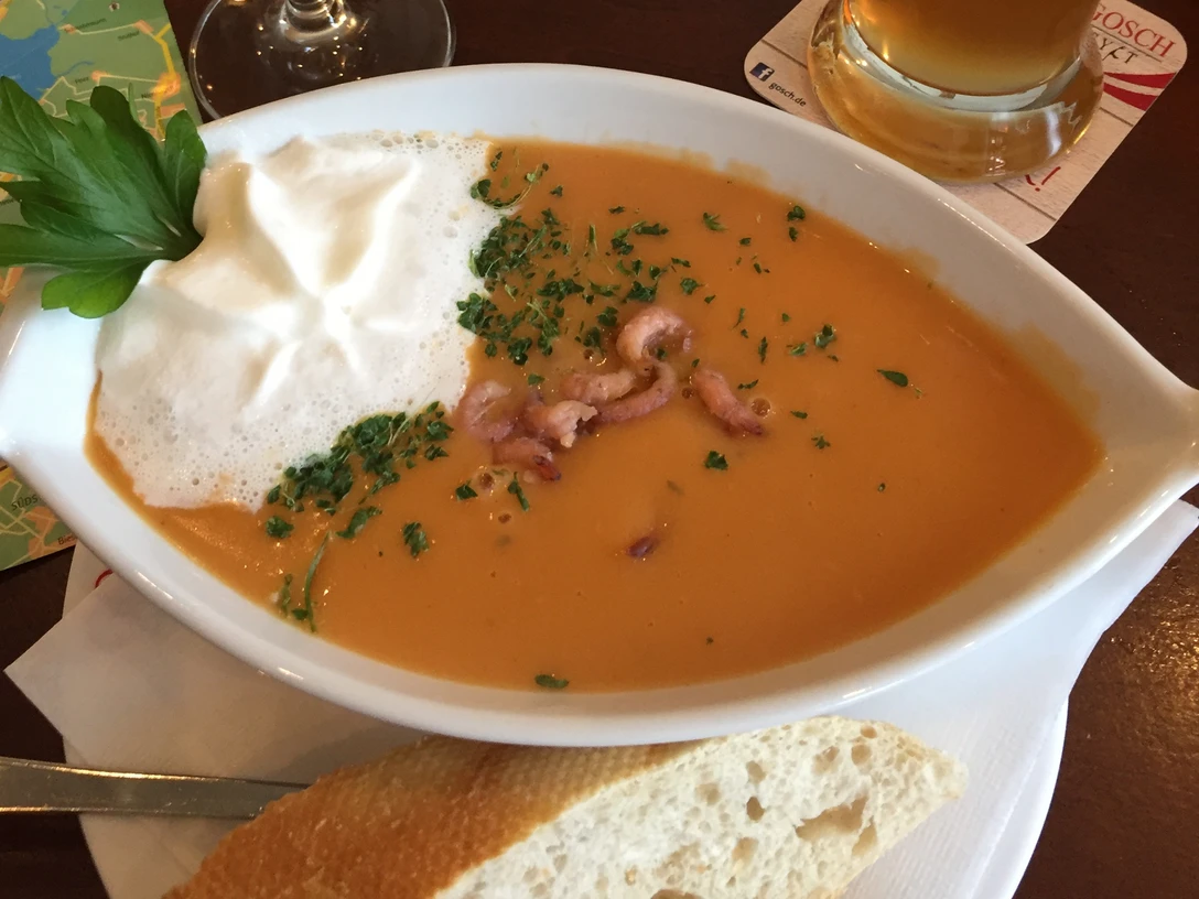 Fischsuppe Cremige Fischsuppe mit Meeresfrüchten und Sahnehaube, serviert mit frischem Baguette auf einem Tisch.Creamy fish soup with seafood and cream topping, served with fresh baguette on a table.Cremet fiskesuppe med skaldyr og fløde, serveret med frisk baguette på et bord.Romige vissoep met zeevruchten en een topping van room, geserveerd op tafel met vers stokbrood.