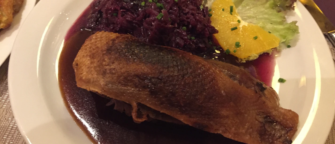 Duck breast on a plate with red cabbage, orange slice and sauce, served with salad garnish.