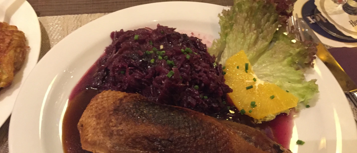 Duck breast in a dark sauce with red cabbage, decorated with salad and orange slices on a plate.