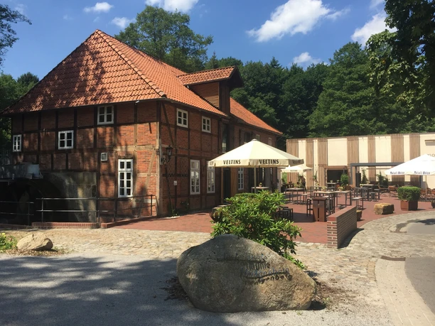 Klostermühle Fachwerkgebäude mit rotem Ziegeldach, Naturumgebung, Außenbereich mit Tischen und Vordach.