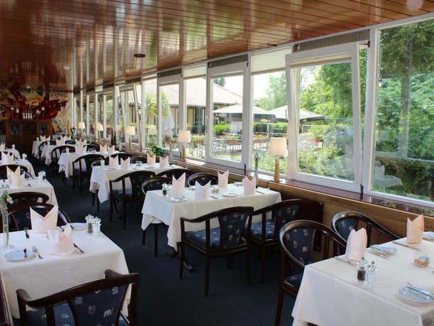 Large restaurant with covered tables, panoramic front and view of the green landscape outside.