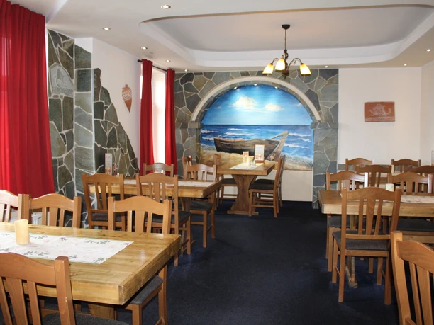 Restaurant Platon Griechisches Restaurant mit Holzmöbeln und Wandgemälde eines Bootes am Strand im Innenbereich.