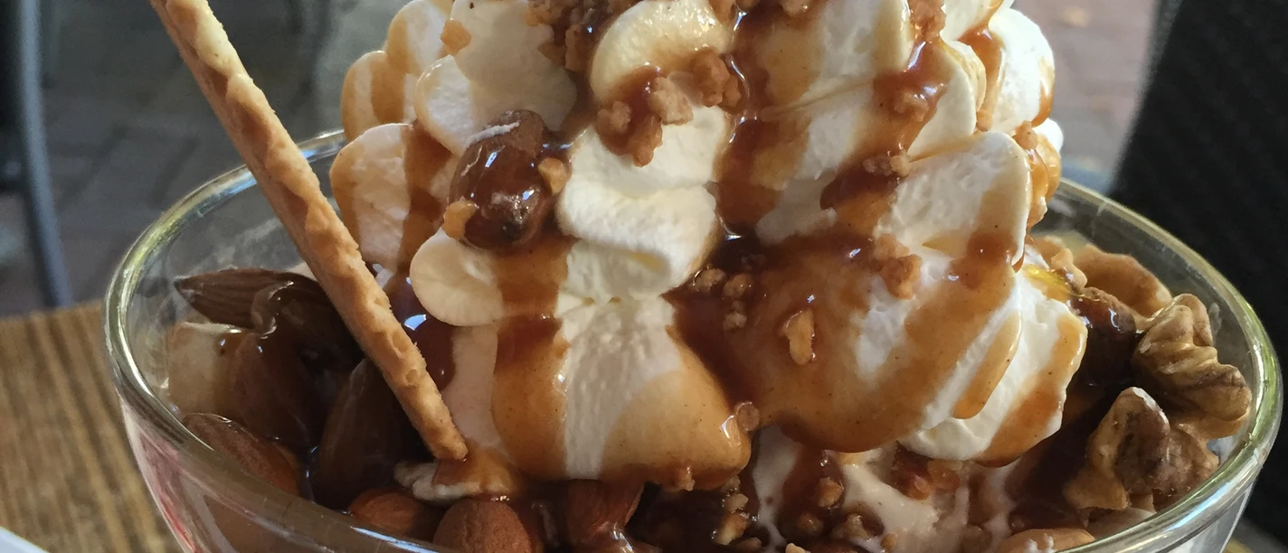 Eisbecher Nuss Köstlicher Eisbecher mit Sahne, Karamellsauce und knackigen Nüssen, serviert in einer Glasvase.