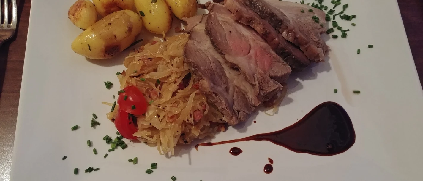 Roast potatoes, juicy pork, sauerkraut with tomatoes and balsamic vinegar decoration on a white plate.