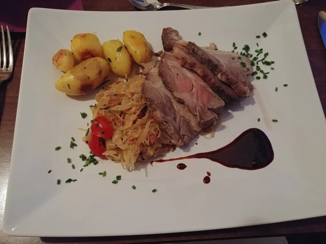 Schwein und Sauerkraut Bratkartoffeln, saftiges Schweinefleisch, Sauerkraut mit Tomaten und Balsamico-Dekor auf weißem Teller.