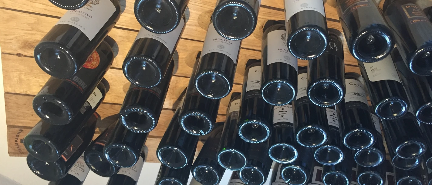 Weinregal Eine Vielzahl von Weinflaschen lagert waagerecht in einem Holzregal mit Blick auf die Flaschenböden.