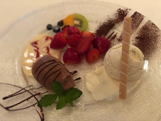 Verschiedene Obstsorten, Vanilleeis, Schokocreme und eine Waffelspirale auf einem Teller arrangiert.
