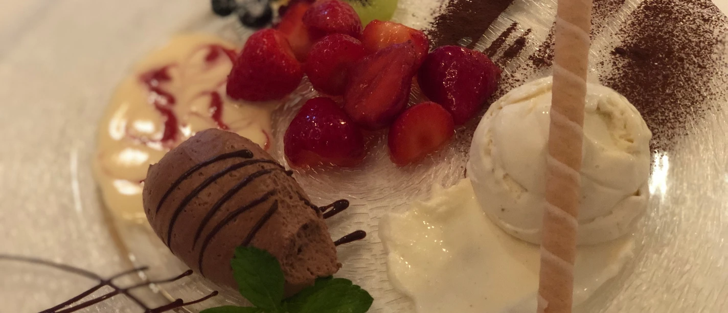 Dessertteller Verschiedene Obstsorten, Vanilleeis, Schokocreme und eine Waffelspirale auf einem Teller arrangiert.
