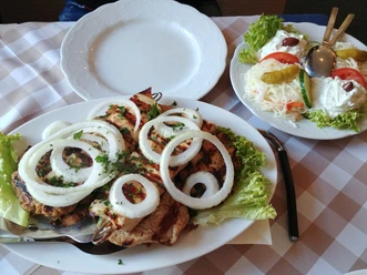griechische Fleischplatte Verschiedene gegrillte Fleischsorten auf einem weißen Teller, garniert mit Zwiebelringen und Petersilie.