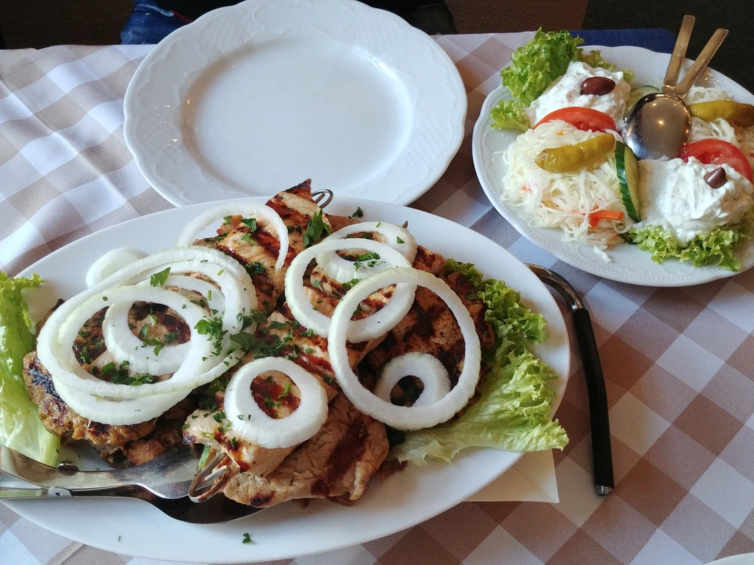 griechische Fleischplatte Verschiedene gegrillte Fleischsorten auf einem weißen Teller, garniert mit Zwiebelringen und Petersilie.