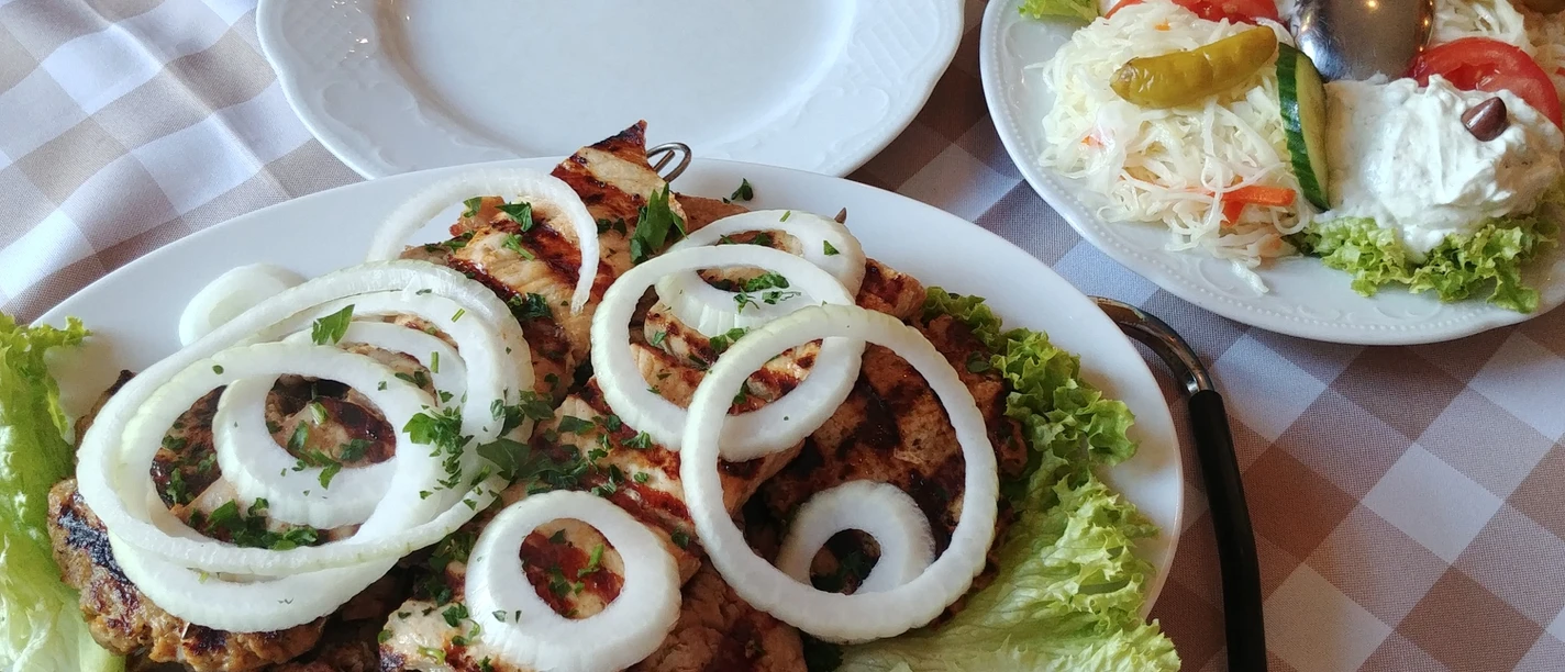 griechische Fleischplatte Verschiedene gegrillte Fleischsorten auf einem weißen Teller, garniert mit Zwiebelringen und Petersilie.