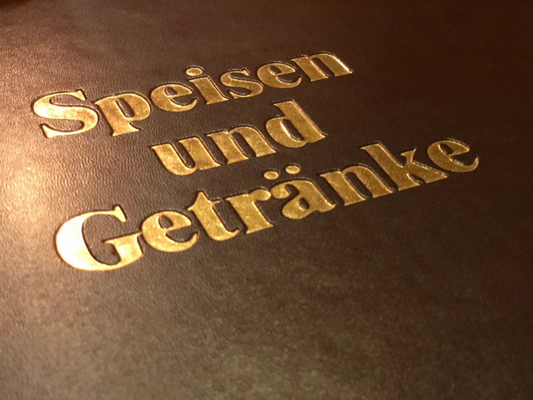 Goldene Buchstaben auf dunklem Hintergrund kennzeichnen die Speisen- und Getränkekarte eines Restaurants.