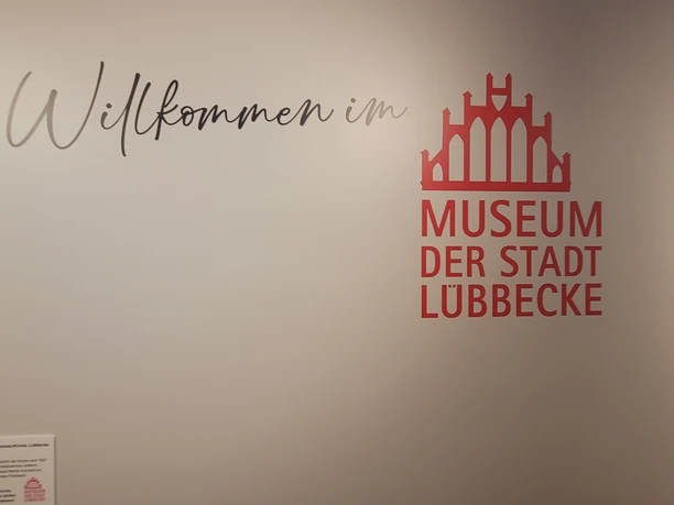 Museum der Stadt Lübbecke Logo und Schriftzug Willkommen im Museum der Stadt Lübbecke an einer weißen Wand.