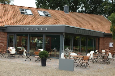 Exterior view of the "Romance" restaurant with terrace seating in front of a brick building.