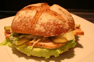A sandwich with fresh ingredients such as salad, gherkins and ham on a light plate.