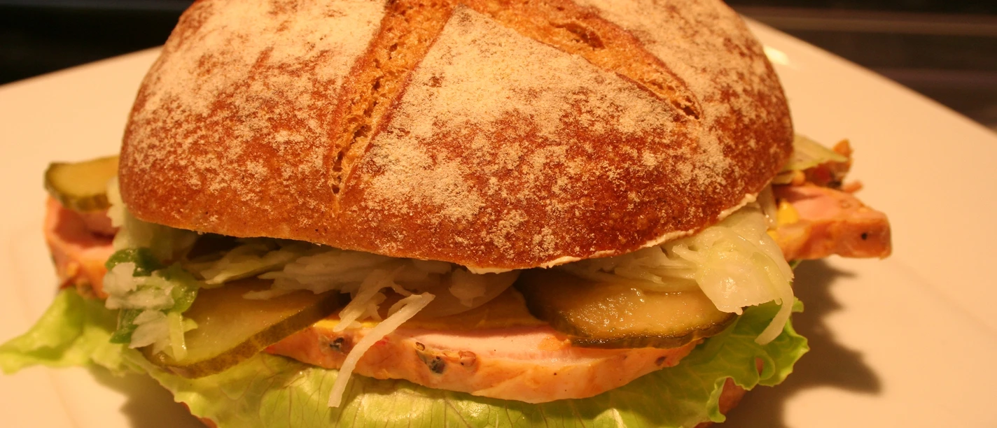 A sandwich with fresh ingredients such as salad, gherkins and ham on a light plate.