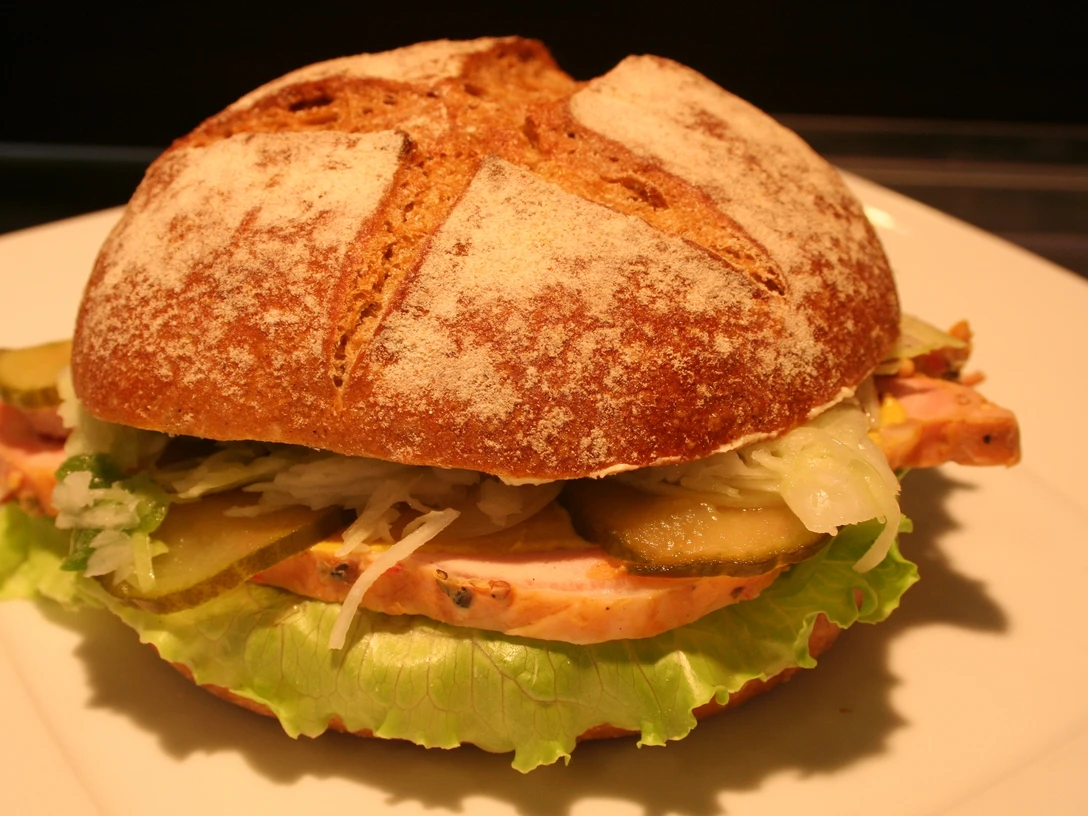 Belegtes Brötchen Ein belegtes Brötchen mit frischen Zutaten wie Salat, Gewürzgurken und Schinken auf hellem Teller.