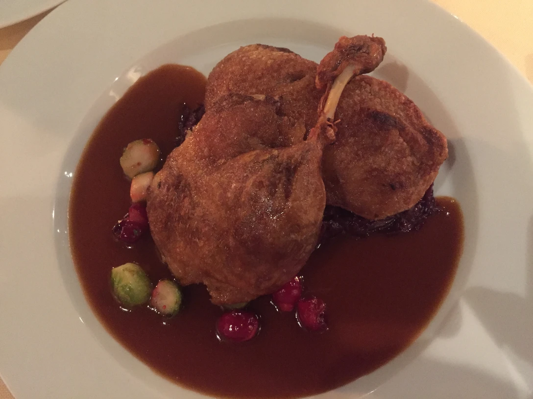 Gans Gericht aus knuspriger Gänsekeule serviert auf dunkler Sauce, verziert mit Rosenkohl und Preiselbeeren.