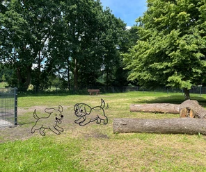 Hundefreilauffläche am Hahnentanger See Eingezäunte Hundefreilauffläche mit Bäumen und Baumstämmen. Zwei gezeichnete Hunde toben.