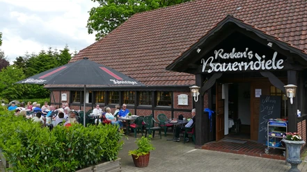Renkens Bauerndiele.jpg Das Restaurant hat eine Terrasse. Viele Gäste sitzen draußen. Es ist ein sonniger Tag.