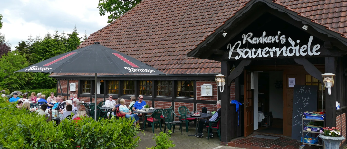 Renkens Bauerndiele.jpg Das Restaurant hat eine Terrasse. Viele Gäste sitzen draußen. Es ist ein sonniger Tag.