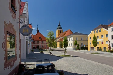 Marktplatz Beratzhausen Marktplatz in Beratzhausen mit Kirche, bunten Häusern und Caféstühlen im Vordergrund.