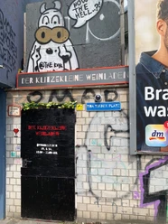 Der Klitzekleine Weinladen Fassade des Klitzekleinen Weinladens mit Graffiti-Kuh und Tina-Turner-Platz-Schild
